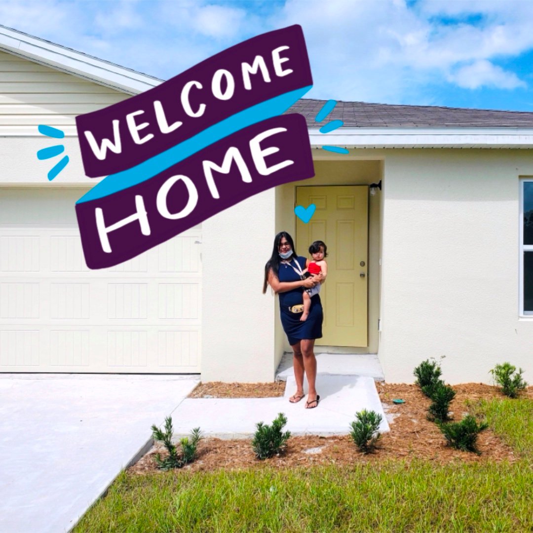 A person holding a baby in front of a house.