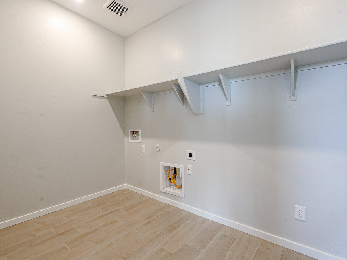 A white room with a wood floor and a white wall with a vent.