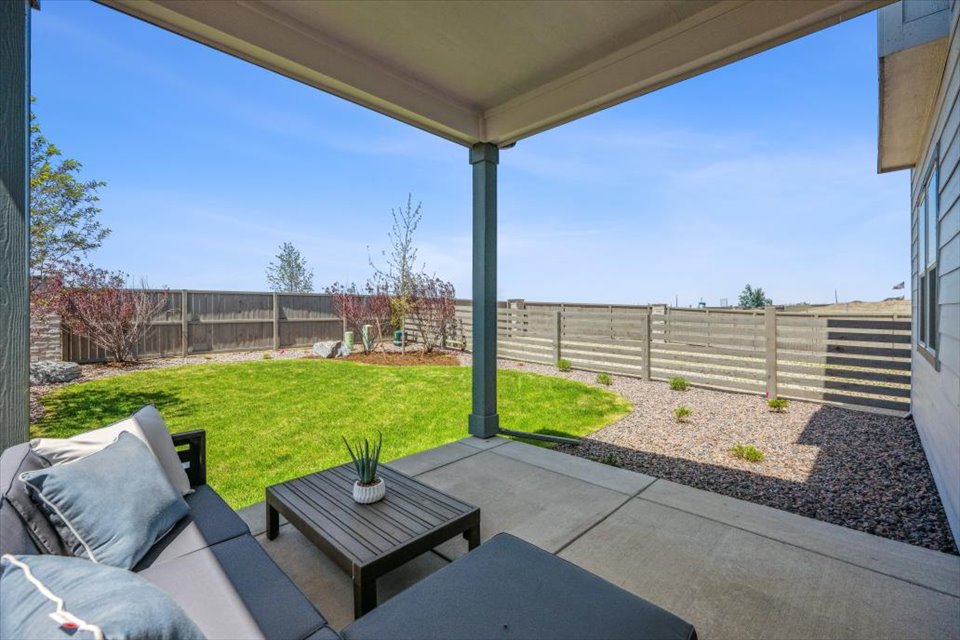 A patio with a table and a couch and a fence and grass.