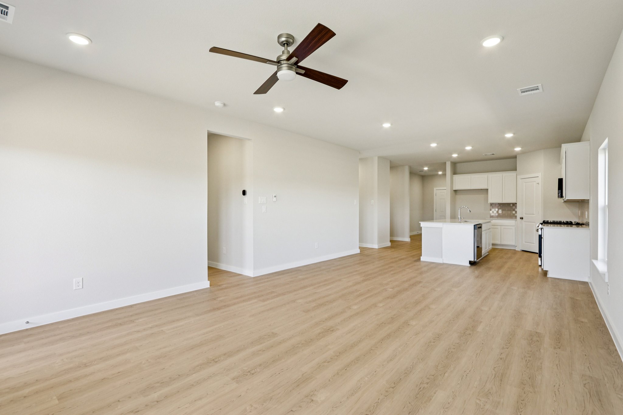 A large empty room with a ceiling fan and a wood floor.