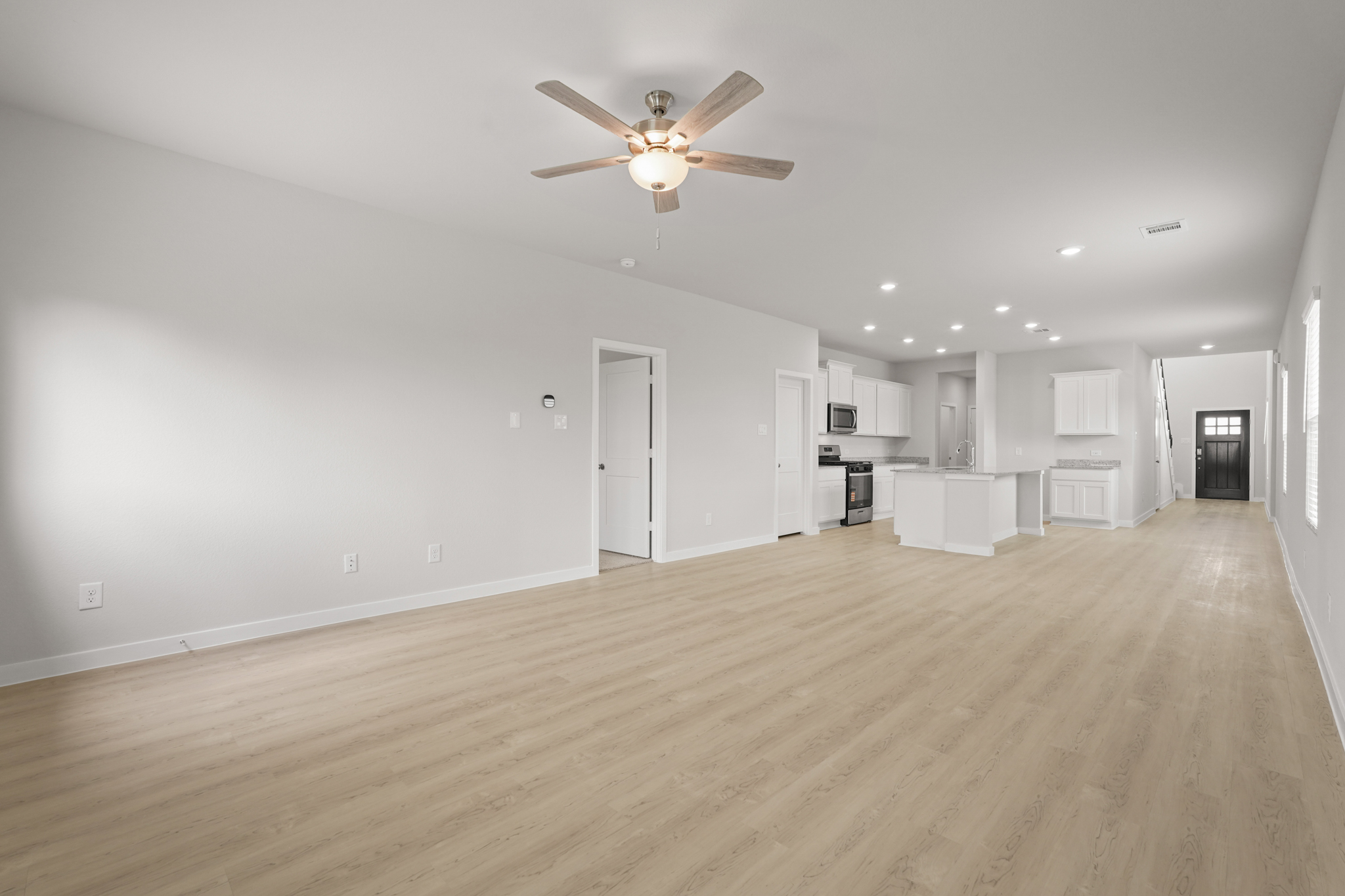 A large empty room with a ceiling fan and a wood floor.